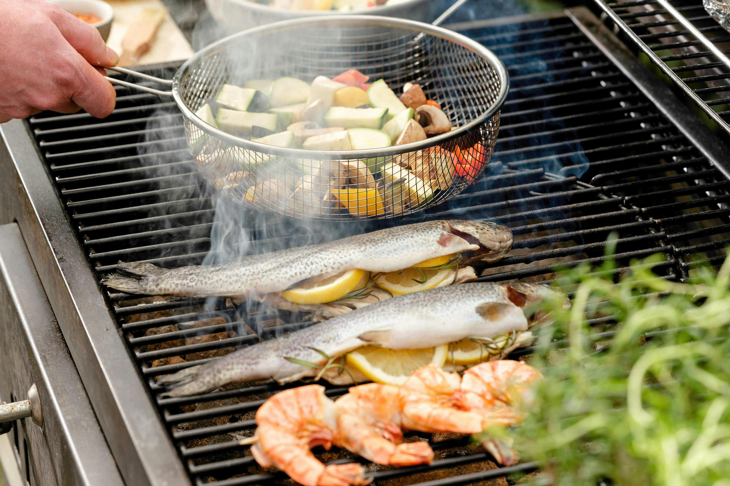 Frying basket with grilled vegetables and trout with lemon on the grill.